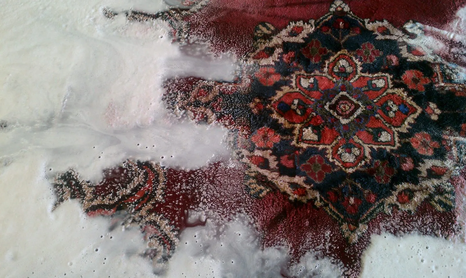 Red Oriental rug mid-wash covered in cleaning foam