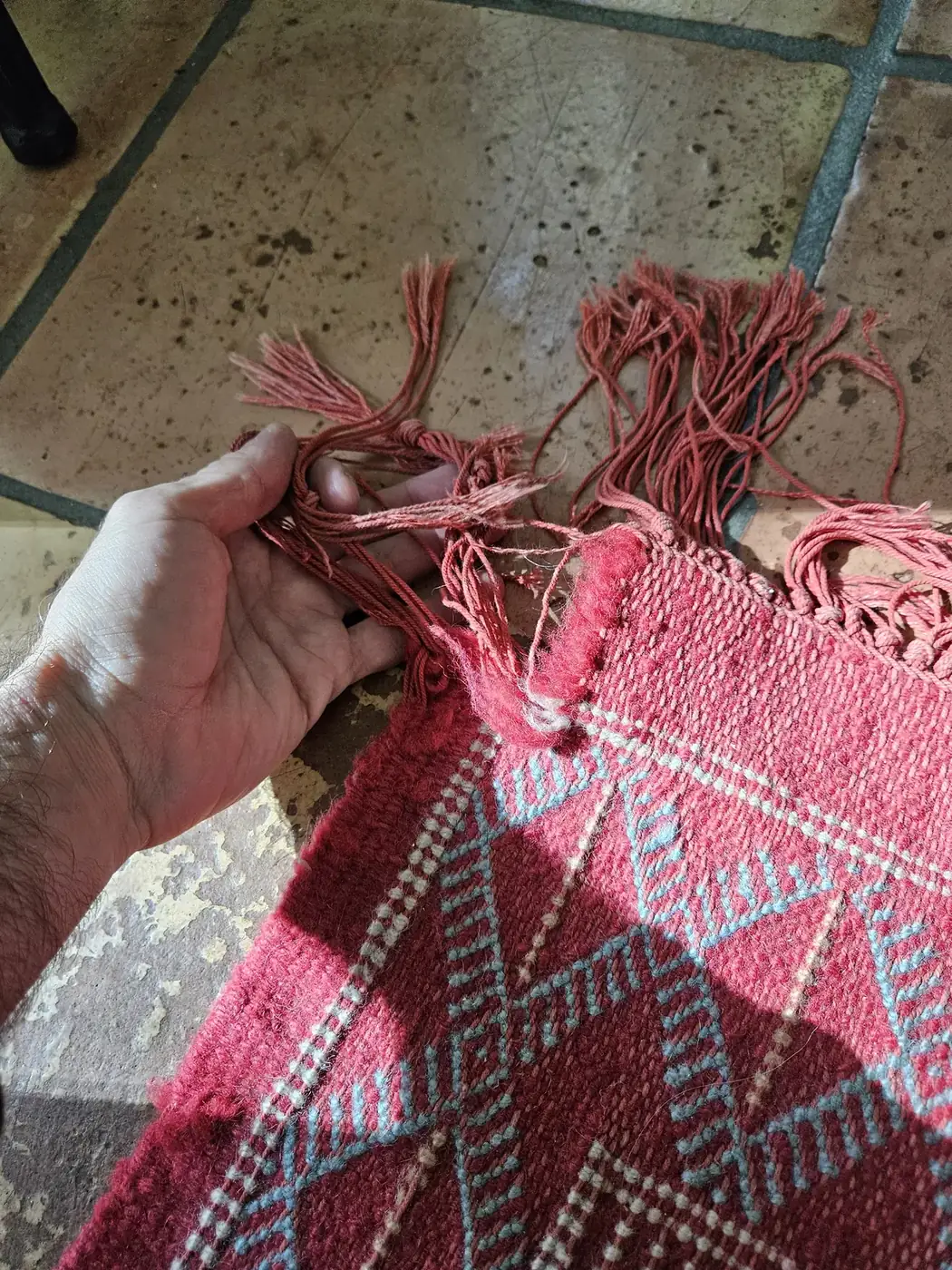Hand holding the damaged fringe of a pink and red tribal rug