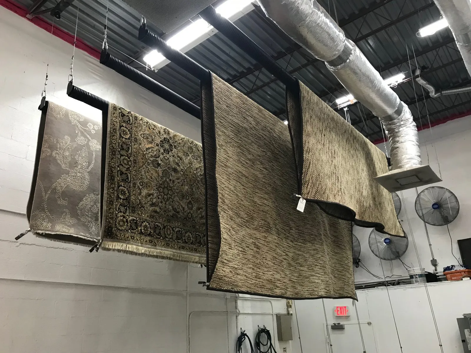 Rugs hanging from ceiling racks in the drying room with circulation fans